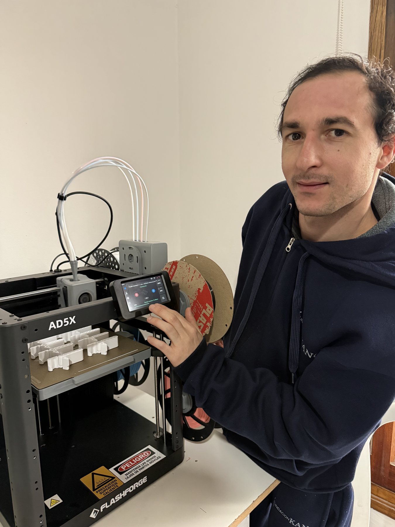 Un alumno junto a una impresora 3D en funcionamiento, sosteniendo una pieza recién terminada.